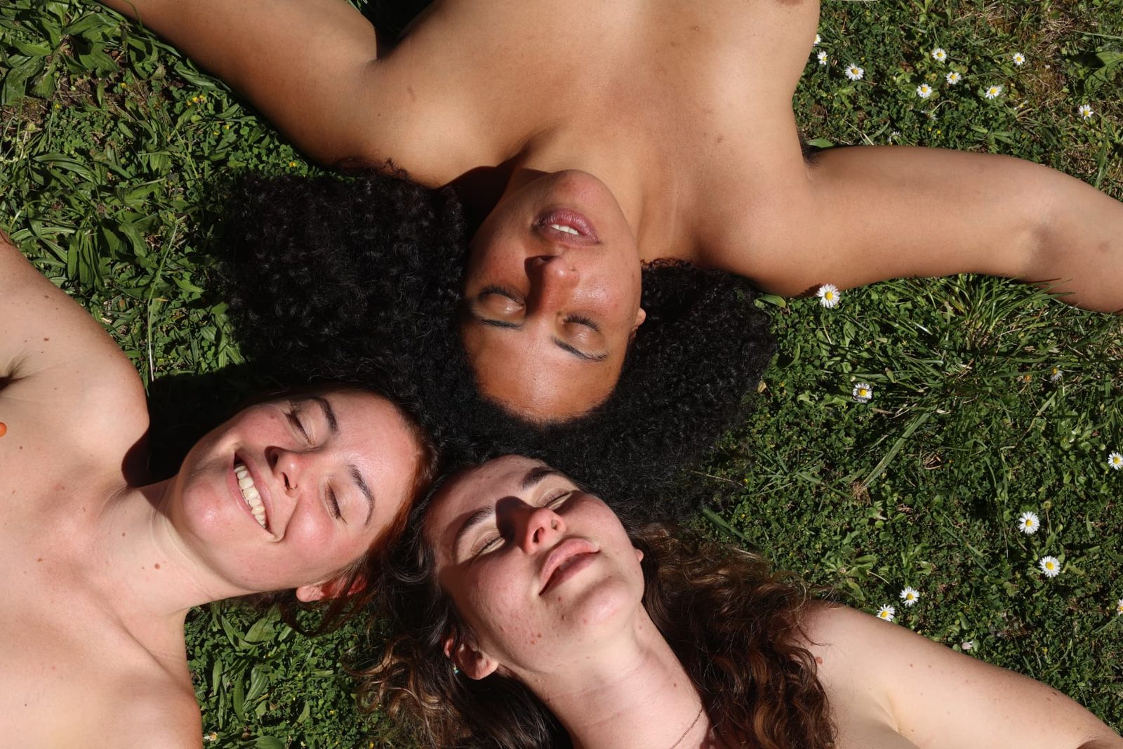 Trois personnes allongées dans l'herbe, visages tournés vers le soleil
