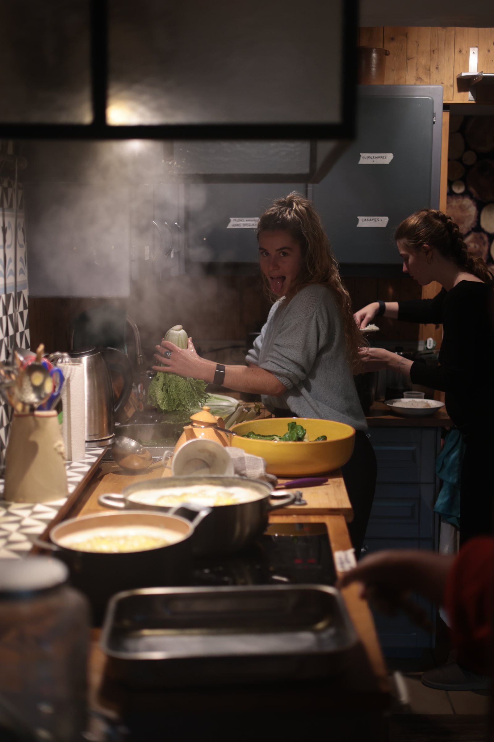 Une habitante cuisinant un grand plat fumant dans la cuisine collective
