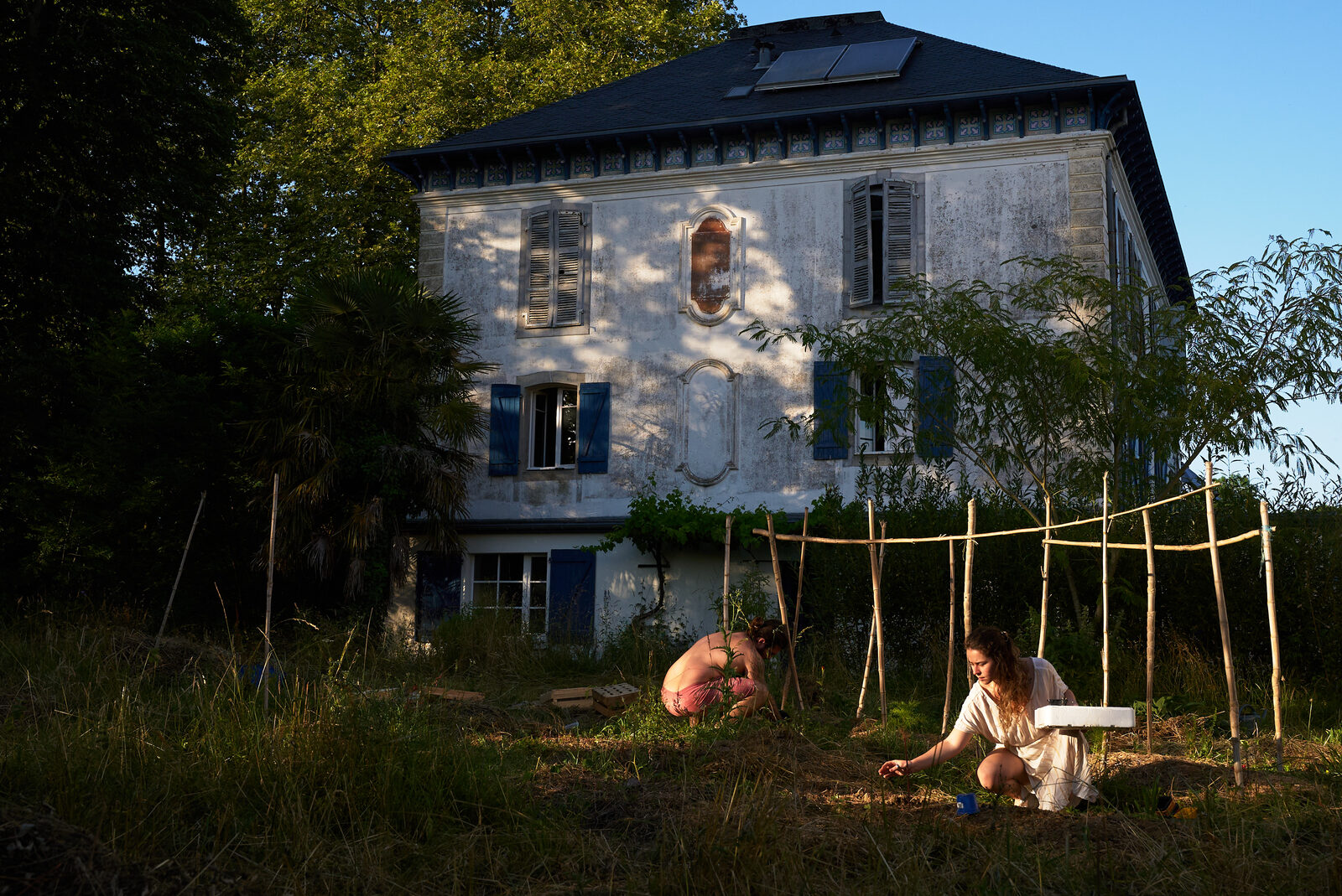 Deux habitantes aménagent le potager devant la maison de maître au soleil couchant